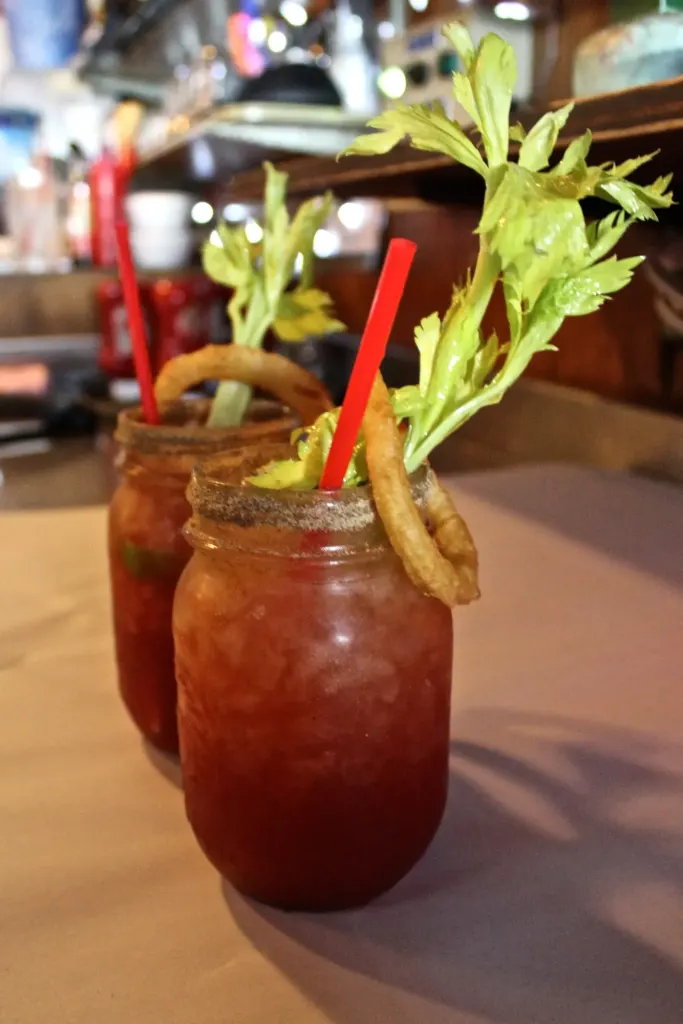 A Caesar in a mason jar with a salted rim, celery, a red straw and an onion ring garnish.