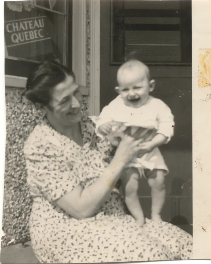 A smiling woman holding a baby on her knee beside a Chateau Quebec sign.