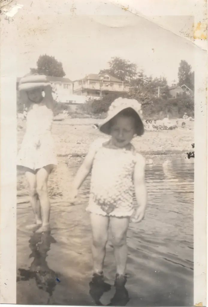 Two young children in sun hats paddling at the water's edge.