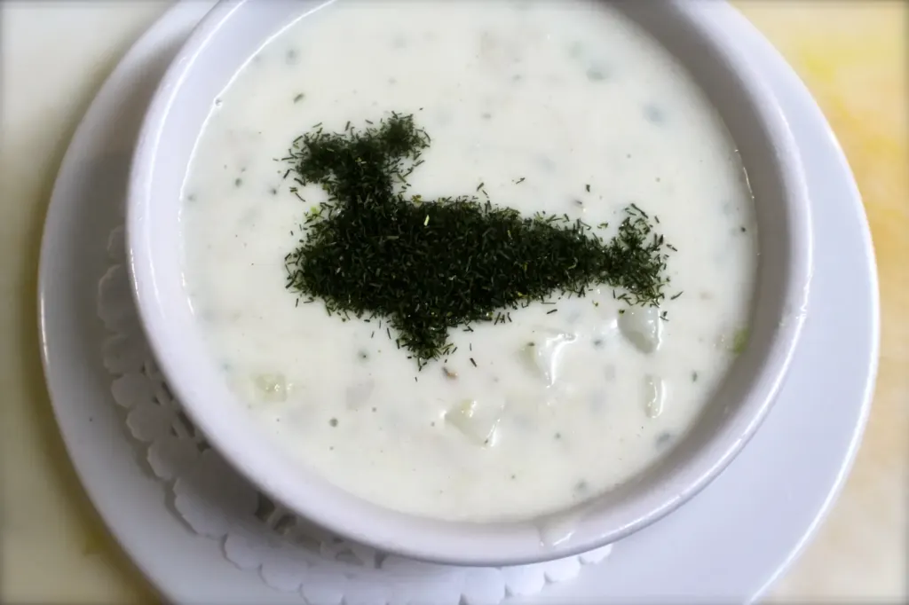 A bowl of creamy clam chowder with dill sprinkled on top in the shape of a whale.