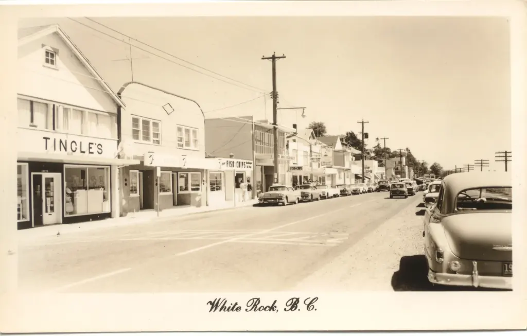 A postcard view of East Marine Drive with Tingle's store and cars parked along the street.