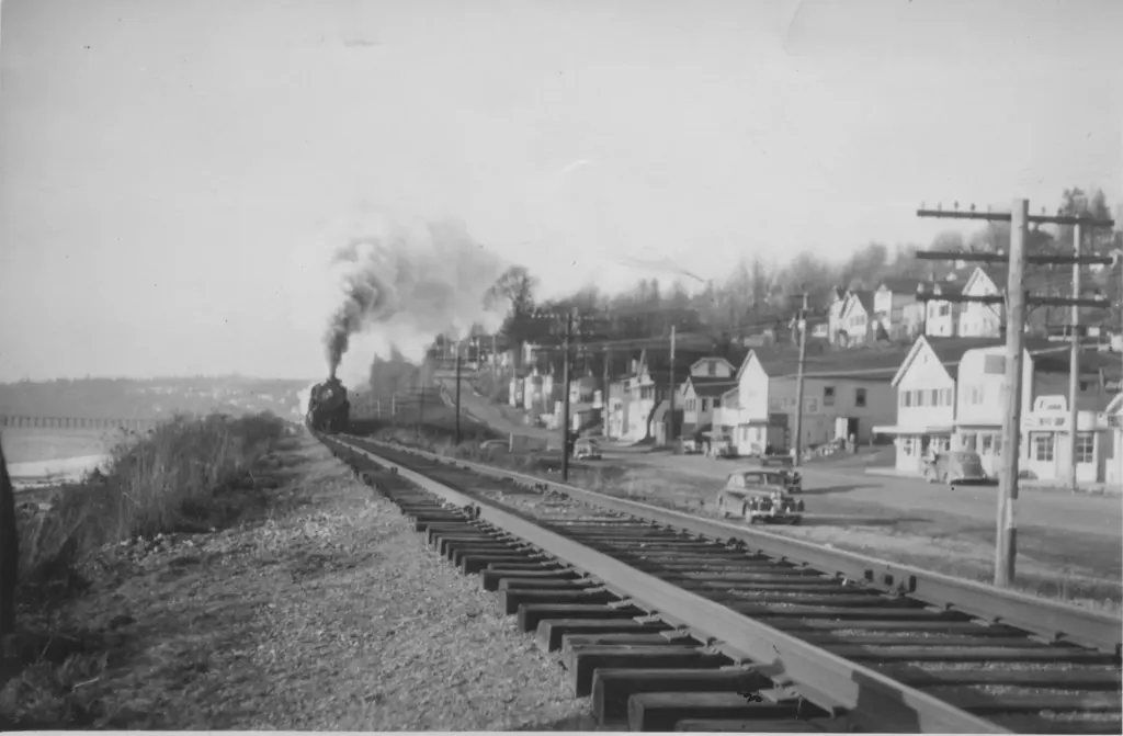 A steam train on the waterfront tracks beside the shops at the east end of White Rock.