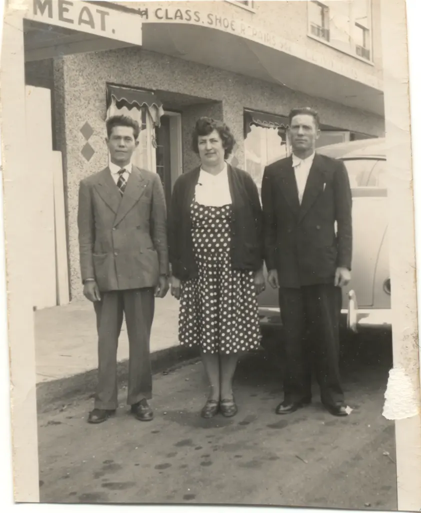 Two men in suits and a woman in a polka-dot dress under signs for Meat and First Class Shoe Repair.