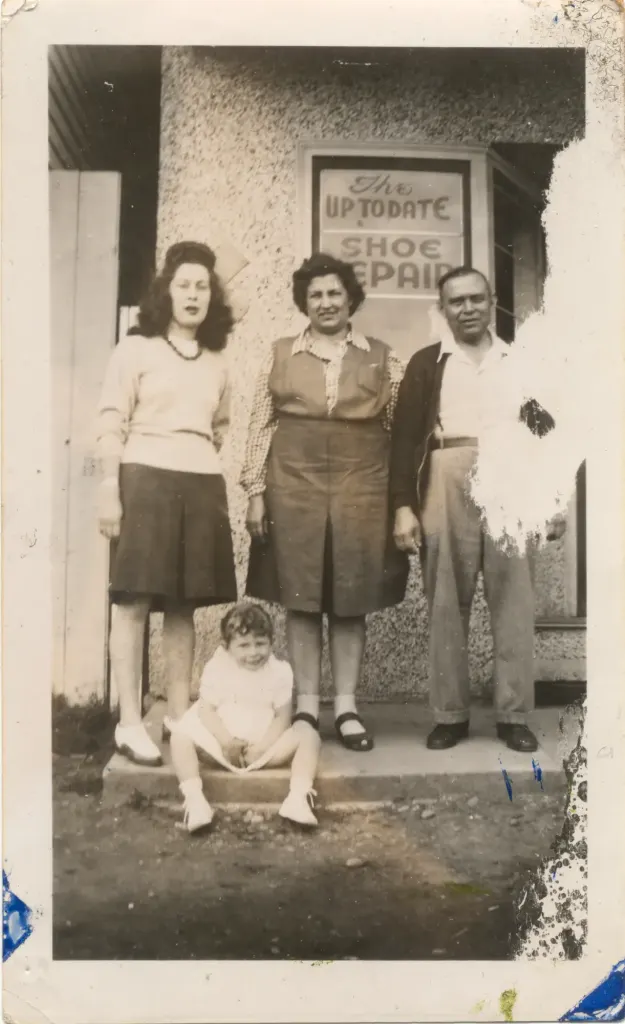 Three adults and a small child in front of the Up-To-Date Shoe Repair window.