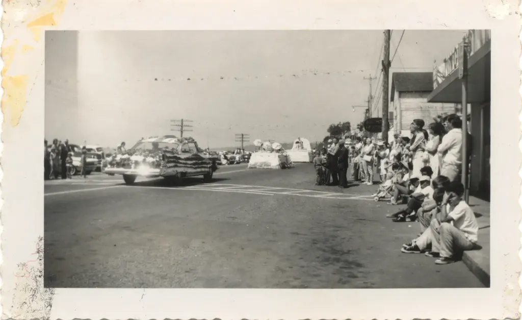 A convertible in a parade, with crowds along the sidewalk.
