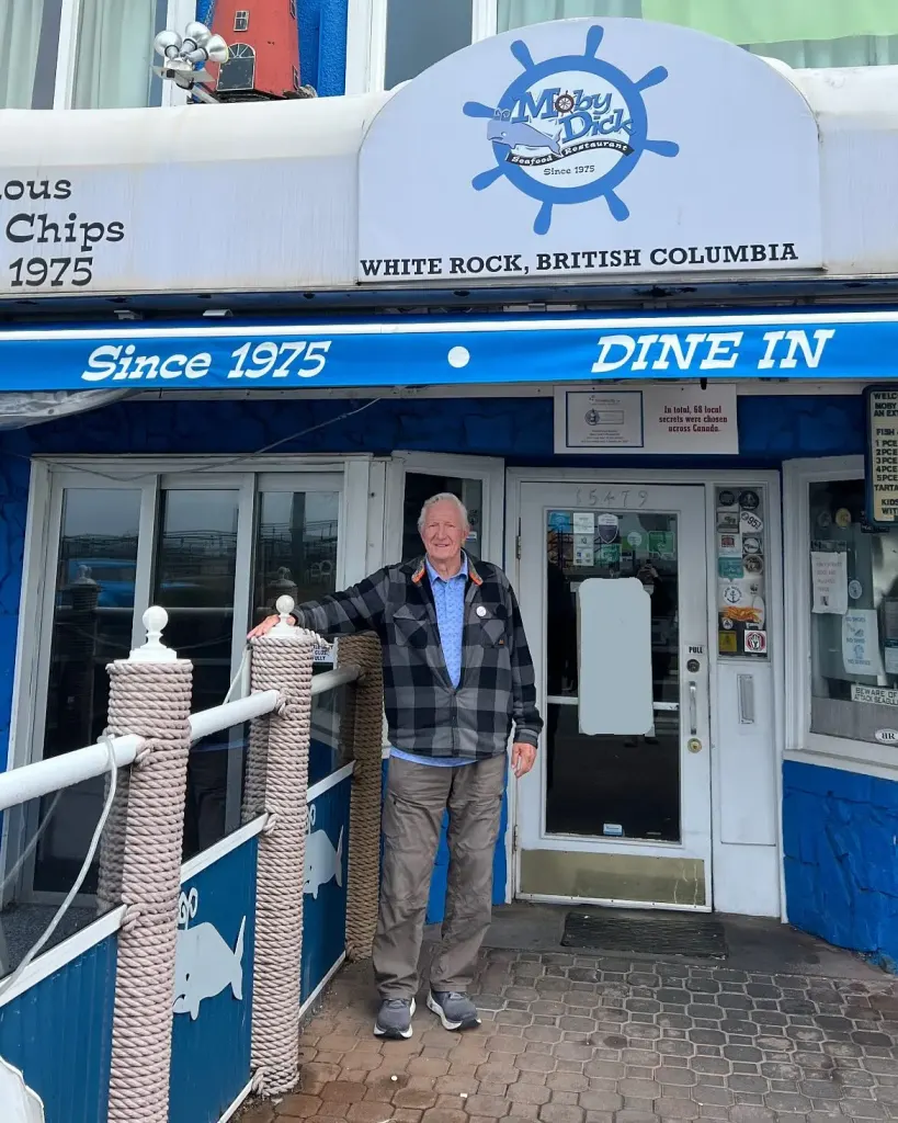 An older man in a plaid jacket stands at the restaurant's front door, under the Since 1975 Dine In awning and the ship's wheel sign.