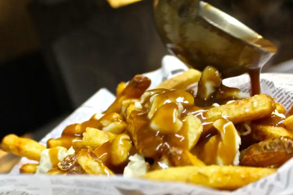 Gravy being poured over a basket of golden fries and cheese curds.