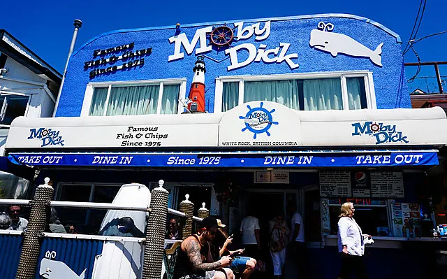 The Moby Dick storefront with its blue sign, lighthouse and whale, and customers on the patio below.