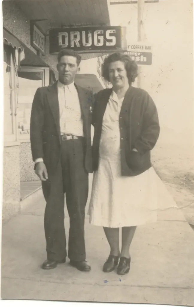A man and a woman standing on the sidewalk under a Drugs sign and a coffee bar sign.